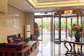 A hotel lobby with a reception desk, seating area, and a glass door leading outside.