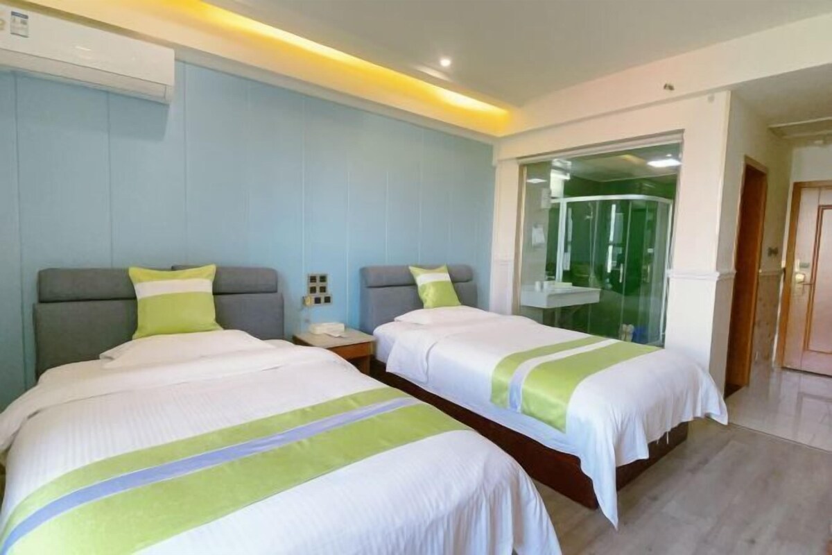 A hotel room with two beds, a glass shower enclosure, and a visible bathroom.