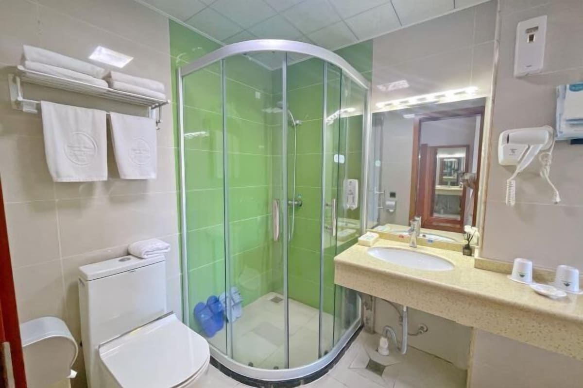 A bathroom with a glass-enclosed shower, a toilet, a sink with a mirror, and a towel rack with towels.
