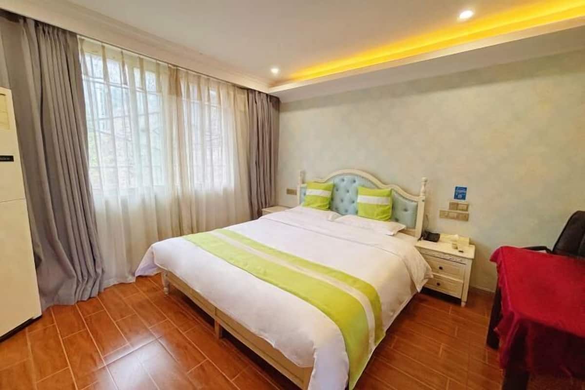 A hotel room with a large bed, a nightstand, a red chair, and a window with curtains.