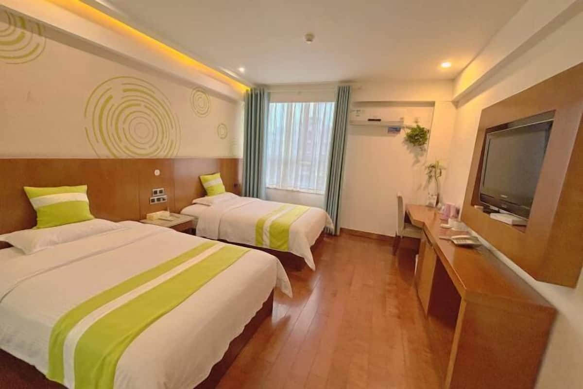 A hotel room with two beds, a desk, a TV, and a window with curtains.