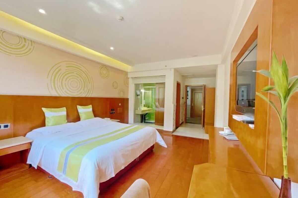 A hotel room with a large bed, a desk, a mirror, and a plant.
