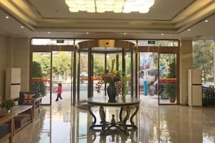 Un vestíbulo de hotel con una puerta giratoria, una mesa redonda con un jarrón de flores y una bandera sobre una mesa.