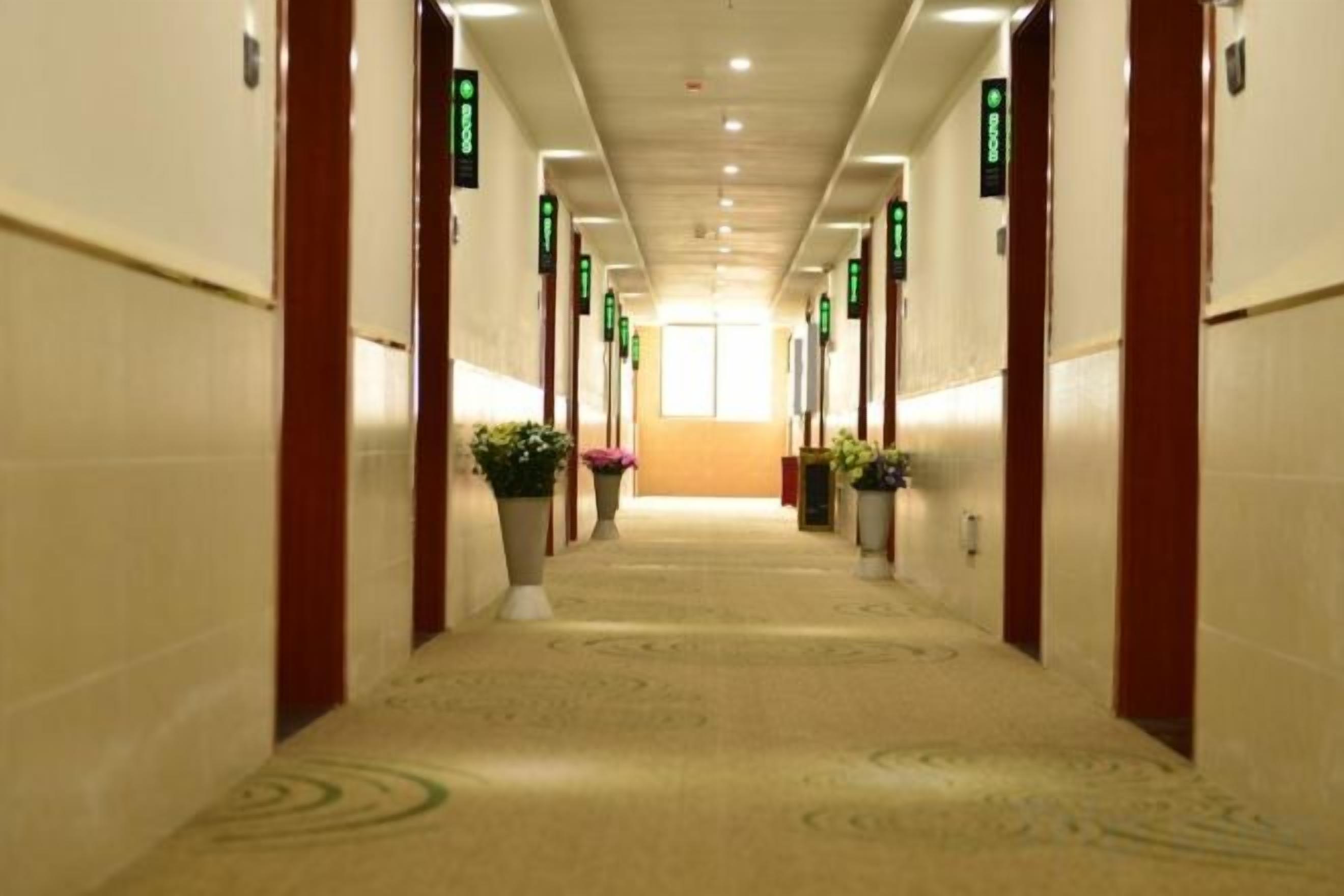 A hotel corridor with carpeted floors, doors on both sides, and green directional signs.