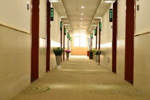 Pasillo de hotel con pisos alfombrados, puertas a ambos lados y señalización direccional verde.