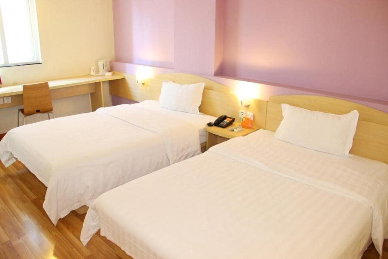 A hotel room with two single beds, a desk, a chair, and a bedside table with a phone and a lamp.