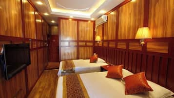 A hotel room with two beds, a television, wooden paneling, and a lamp.
