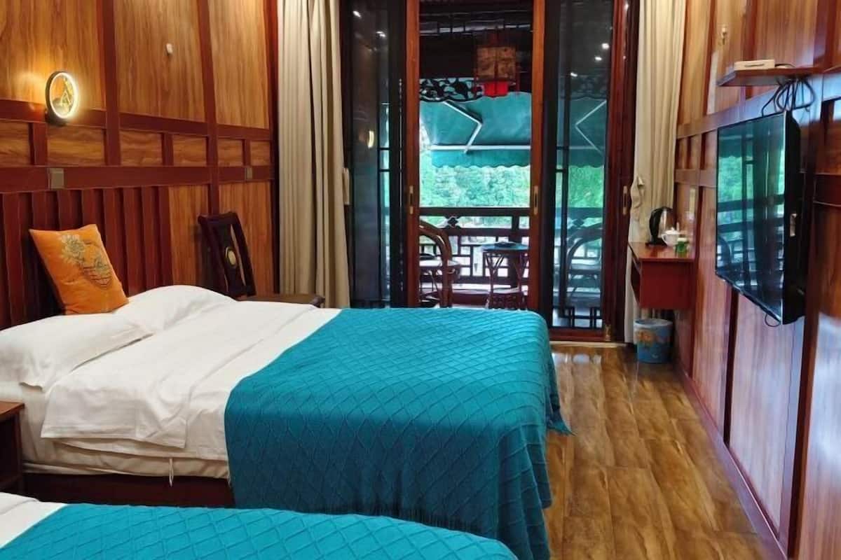 A room with two beds, wooden paneling, a TV, and a balcony with outdoor seating.