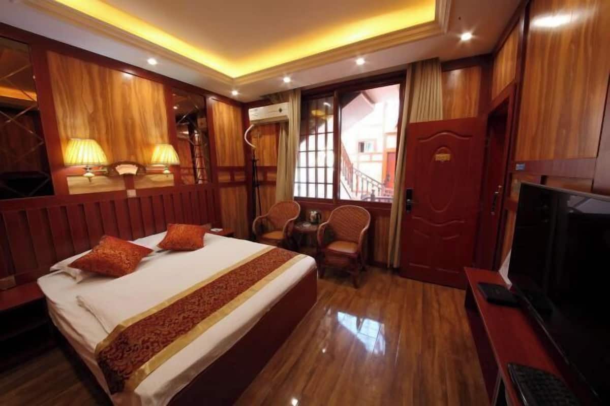 A hotel room with a bed, wooden paneling, a TV, a desk, and a chair.