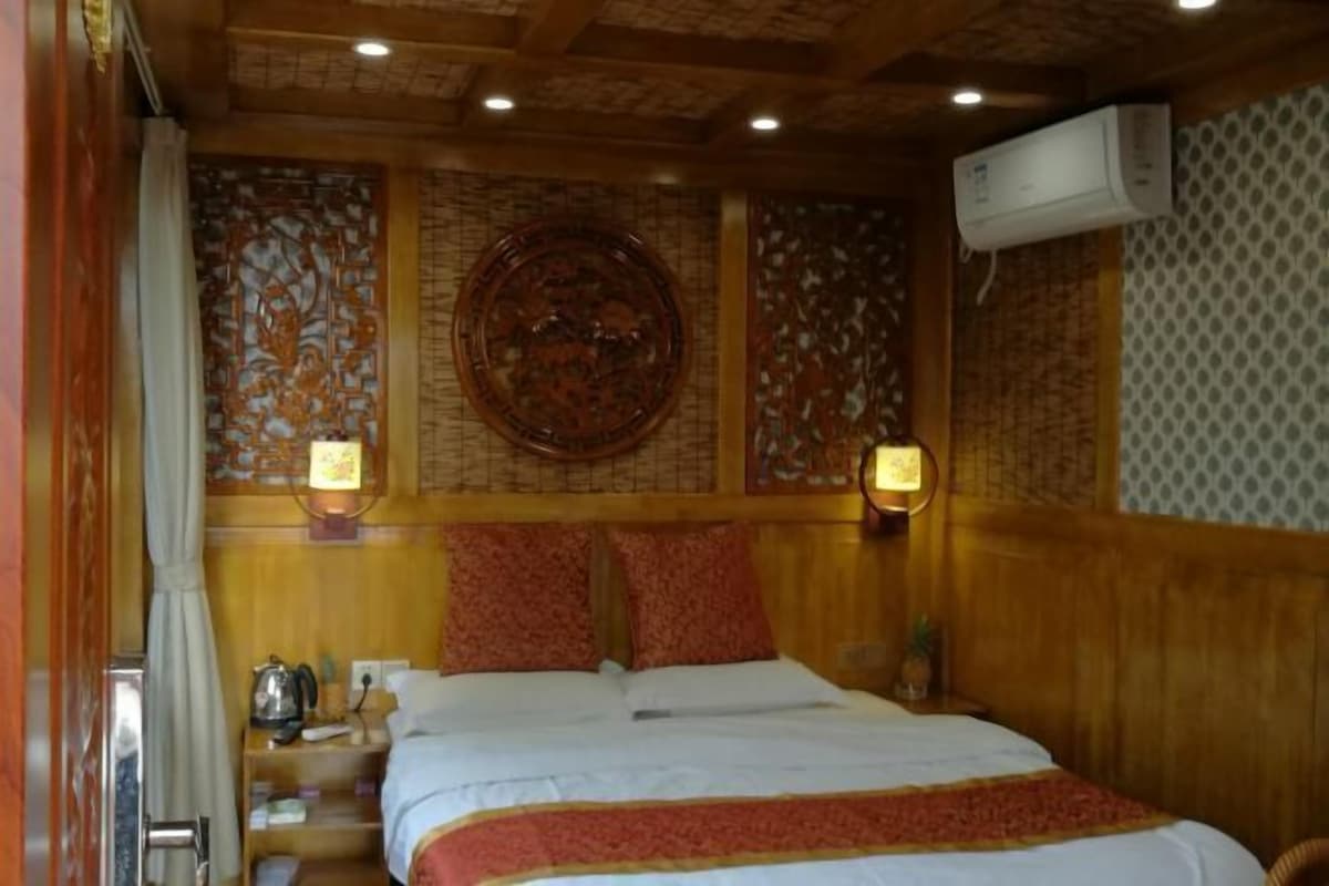 A hotel room with a wooden headboard, a bed with white bedding, two wall-mounted lamps, and a decorative wall panel.