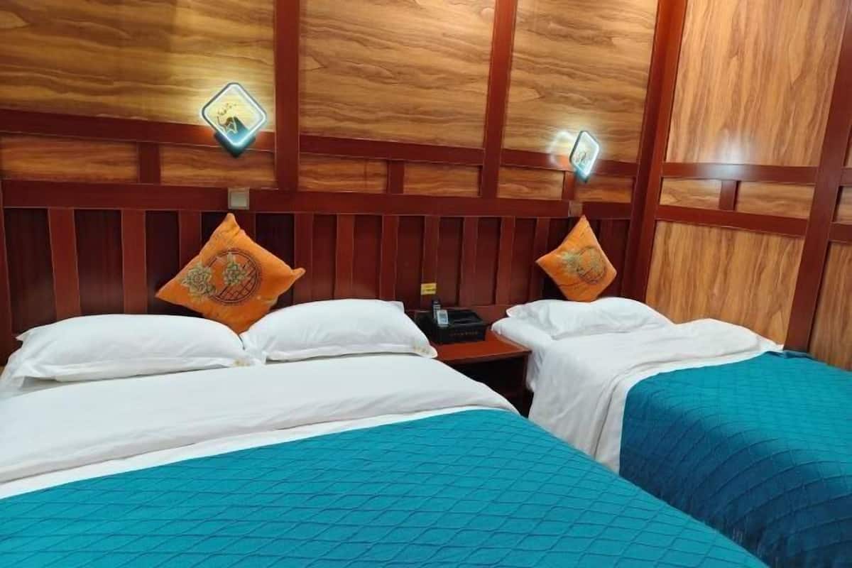 A hotel room with two beds, wooden paneling on the walls, and two wall-mounted lamps.