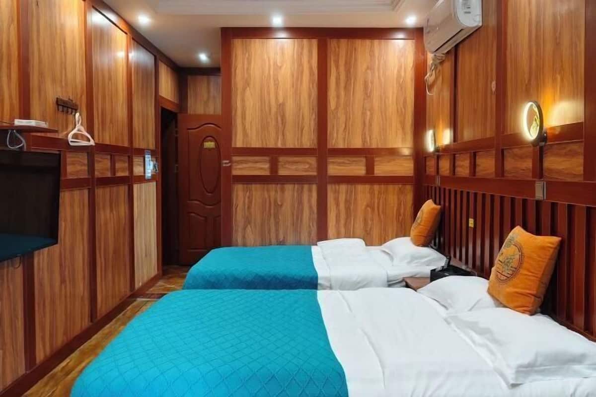 A hotel room with wooden paneling, two beds with blue and white bedding, a TV, and a wardrobe.