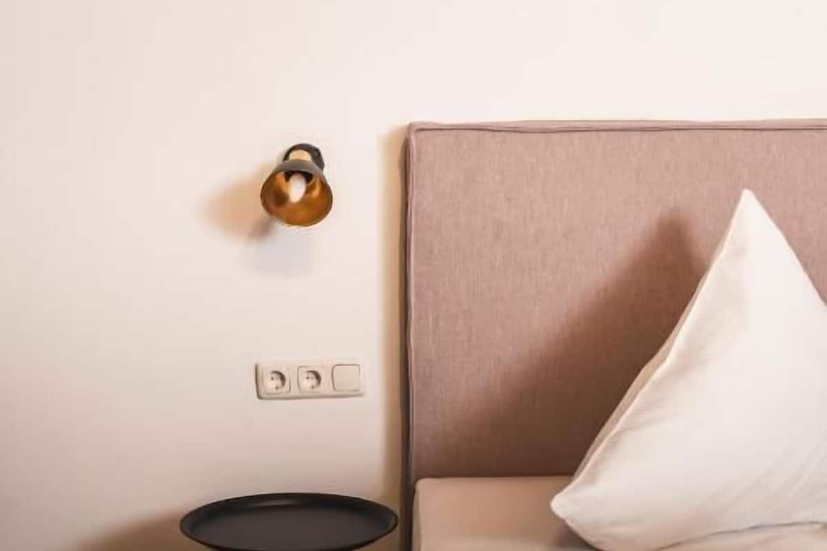 A hotel room with a bed, a bedside table, a lamp, and a power outlet on the wall.