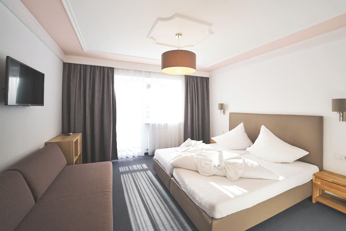 A hotel room with a bed, a sofa, a TV, and a ceiling light.