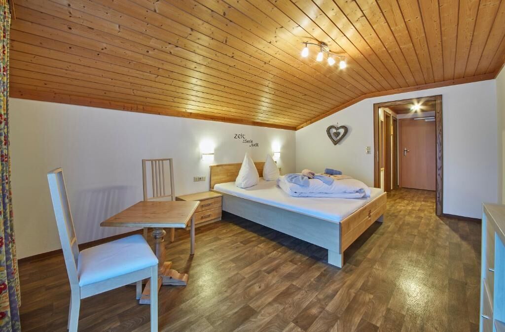 Un dormitorio con techo de madera, una cama con almohadas, una mesita de noche y una silla.