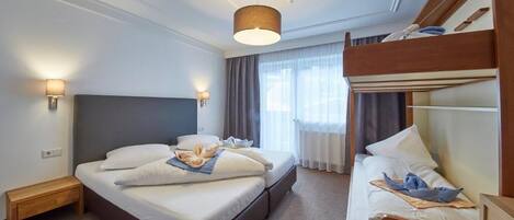 A hotel room with a single bed, a bunk bed, a bedside table, a lamp, and a window with curtains.