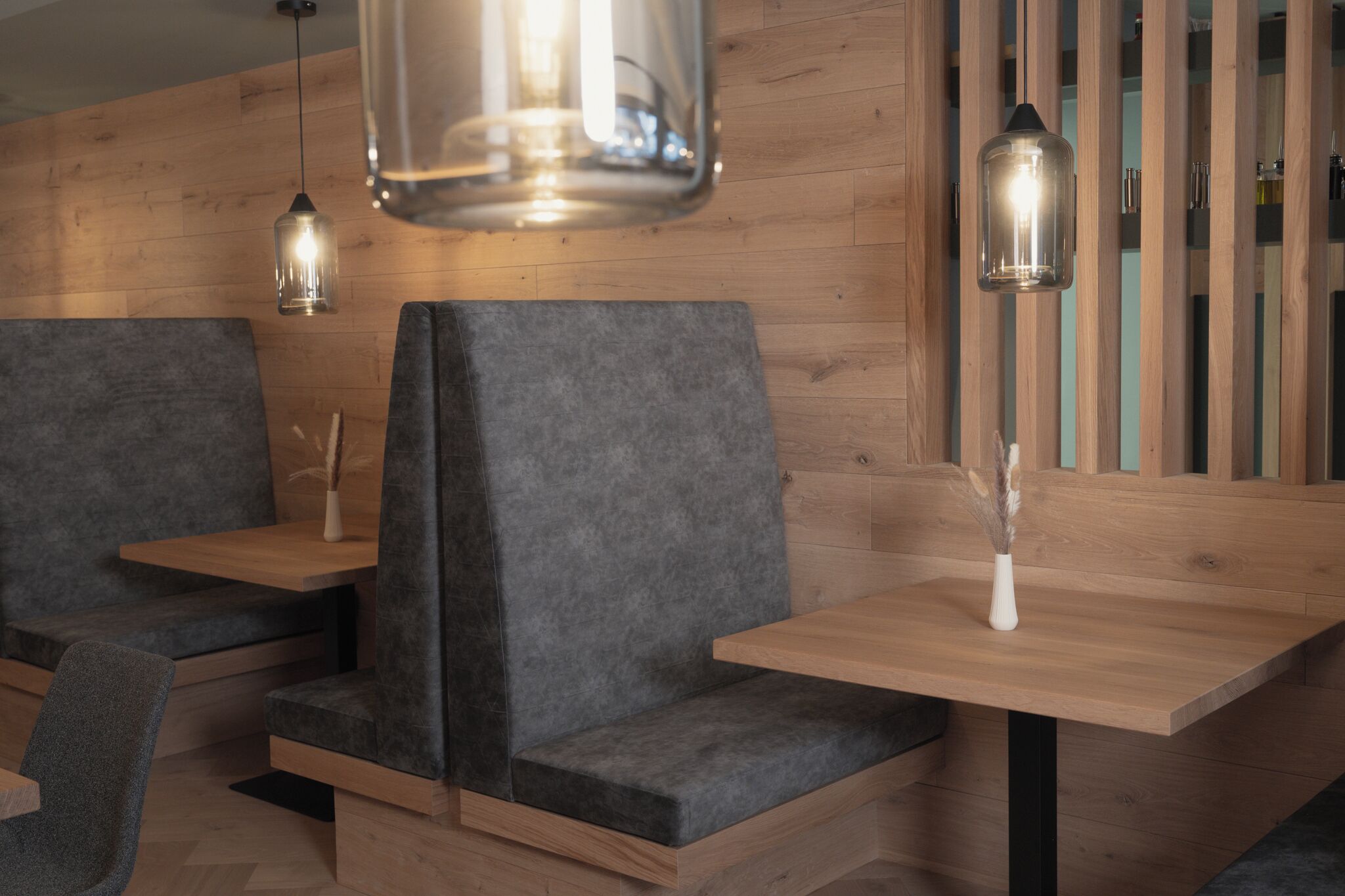 A modern interior with wooden panel walls, grey upholstered seating, and pendant lighting.