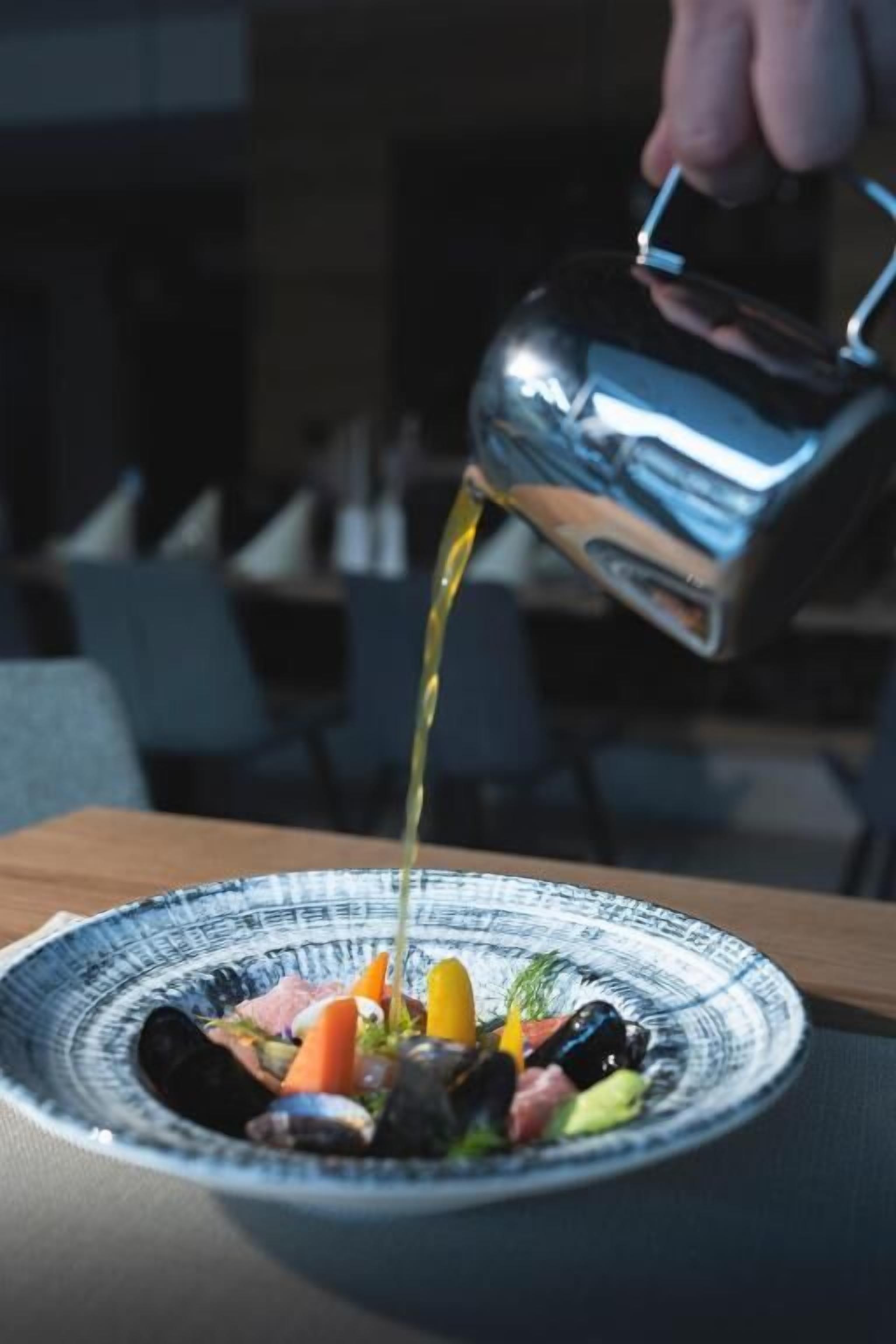 A person pouring a liquid from a metal pitcher onto a plate of food.