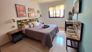 Une chambre à coucher comprenant un lit, une table de chevet, un bureau, une chaise, un ventilateur de plafond et une fenêtre.