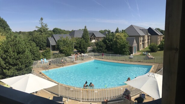 Una piscina con un deck cercado, rodeada de árboles y edificios residenciales.