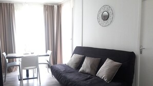Una sala de estar moderna con un sofá oscuro, dos sillas blancas, una mesa de comedor y un adorno mural geométrico.