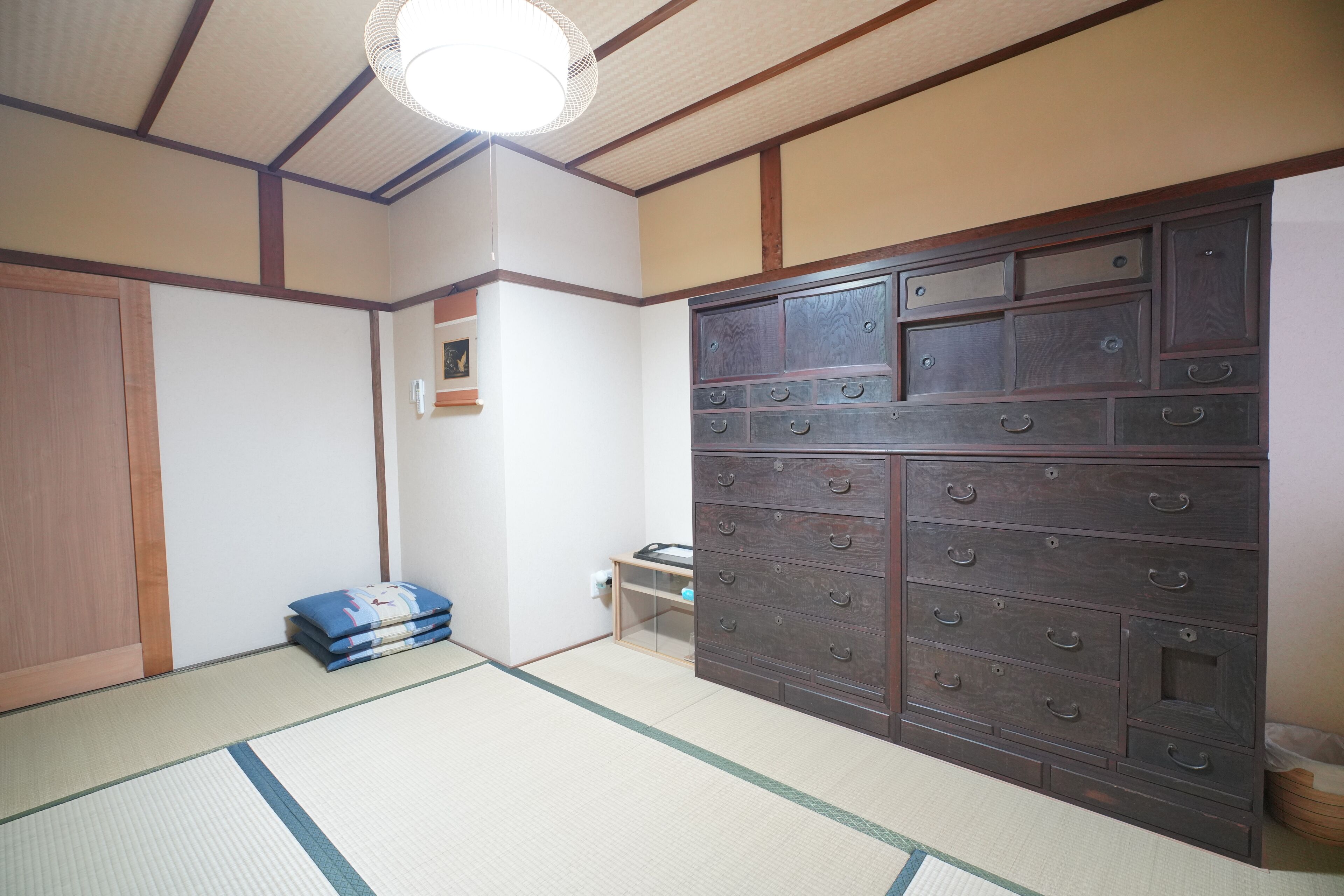 Una habitación japonesa tradicional con suelo de tatami, un amplio armario de madera con varios cajones y una lámpara en el techo.