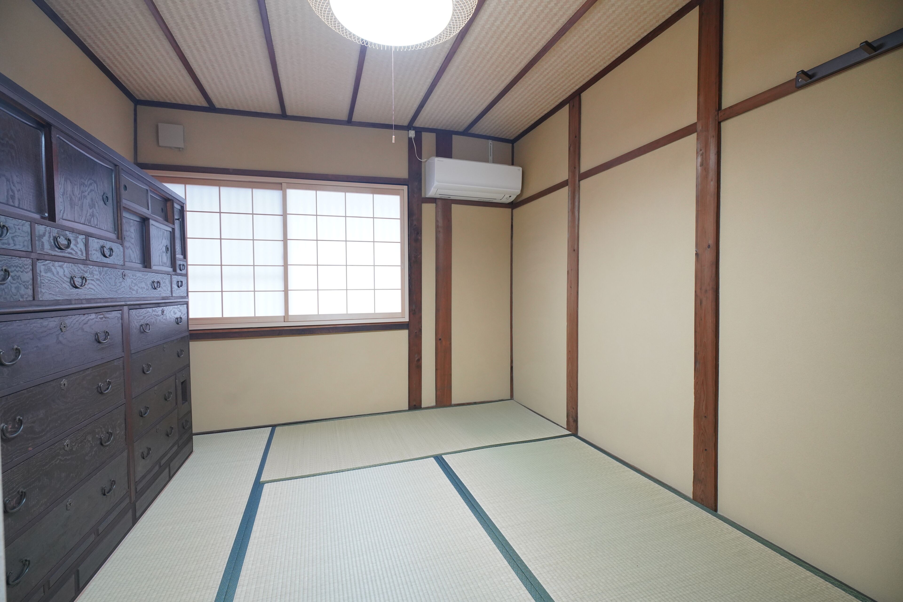 Ein traditioneller japanischer Raum mit Tatami-Boden, einer Schiebetür, einem hölzernen Lowboard und einem Fenster mit Aussicht.