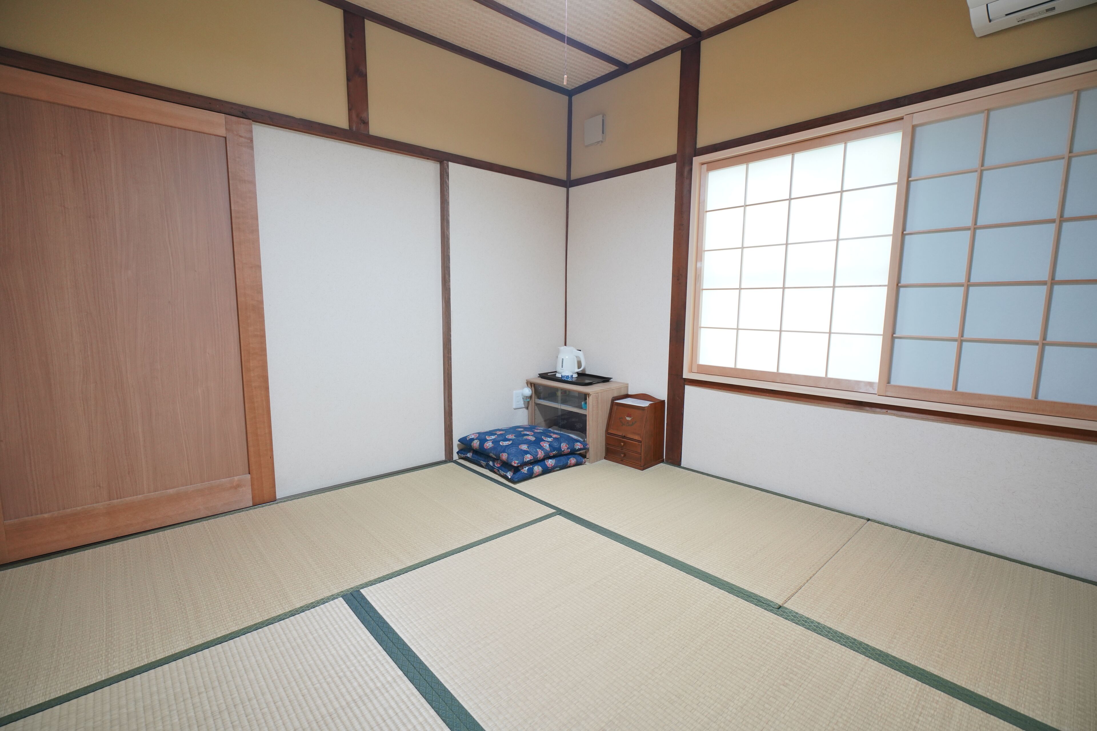 Una habitación japonesa tradicional con suelo de tatami, una puerta corredera, una mesita con un hervidor y una ventana con diseño de cuadrícula.