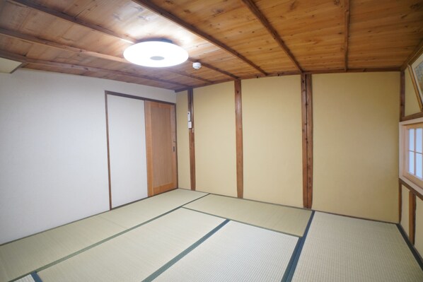Una habitación con suelo de tatami, vigas de madera en el techo y una puerta corrediza.