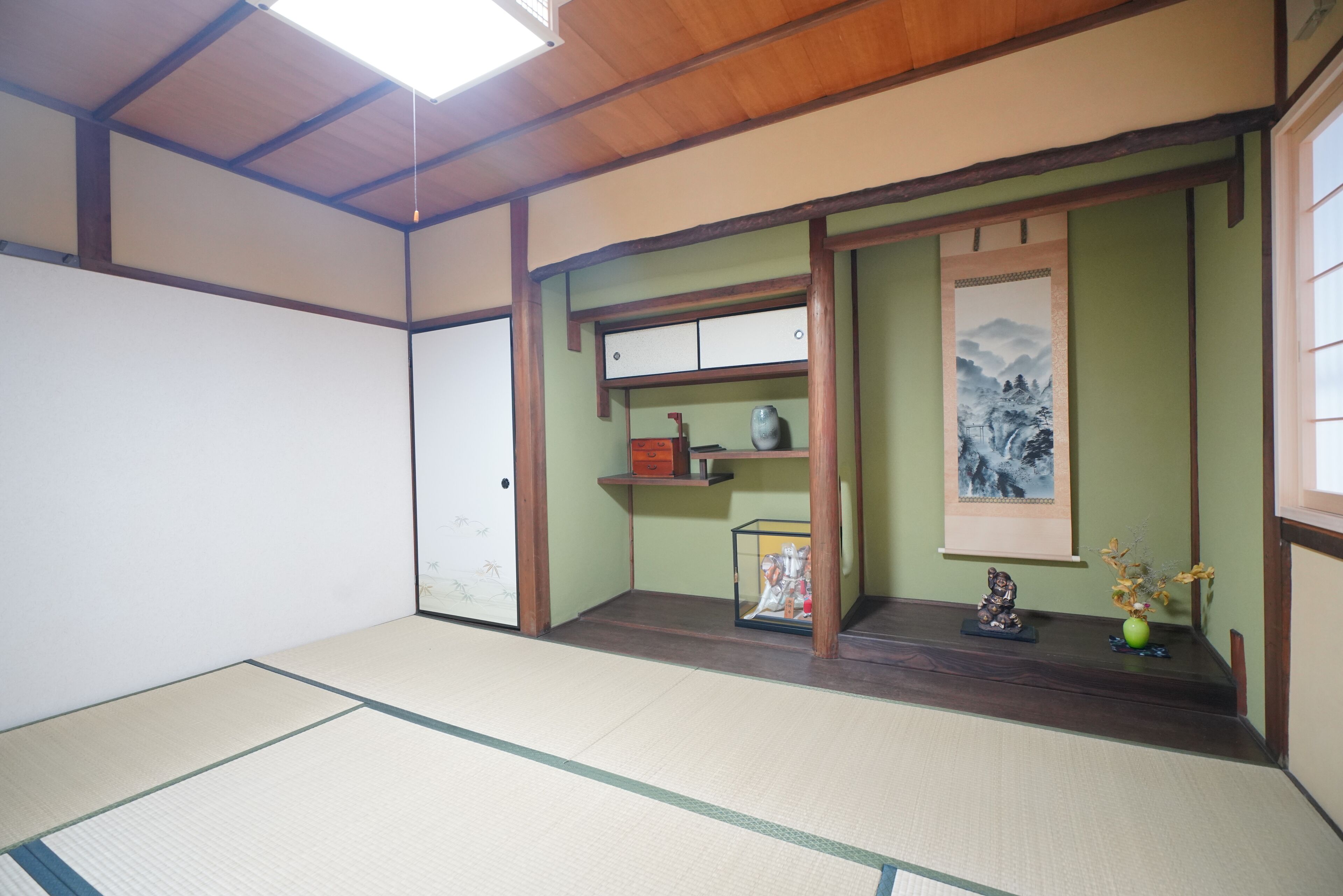 Una habitación con suelo de tatami, una puerta corredera, una estantería con un jarrón y un cuadro en la pared.