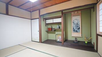 Una habitación con suelo de tatami, una puerta corredera, una estantería con un jarrón y un cuadro en la pared.
