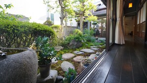 A traditional Japanese garden with a wooden walkway, rocks, and various plants. - Uji Tea Inn (Uji)