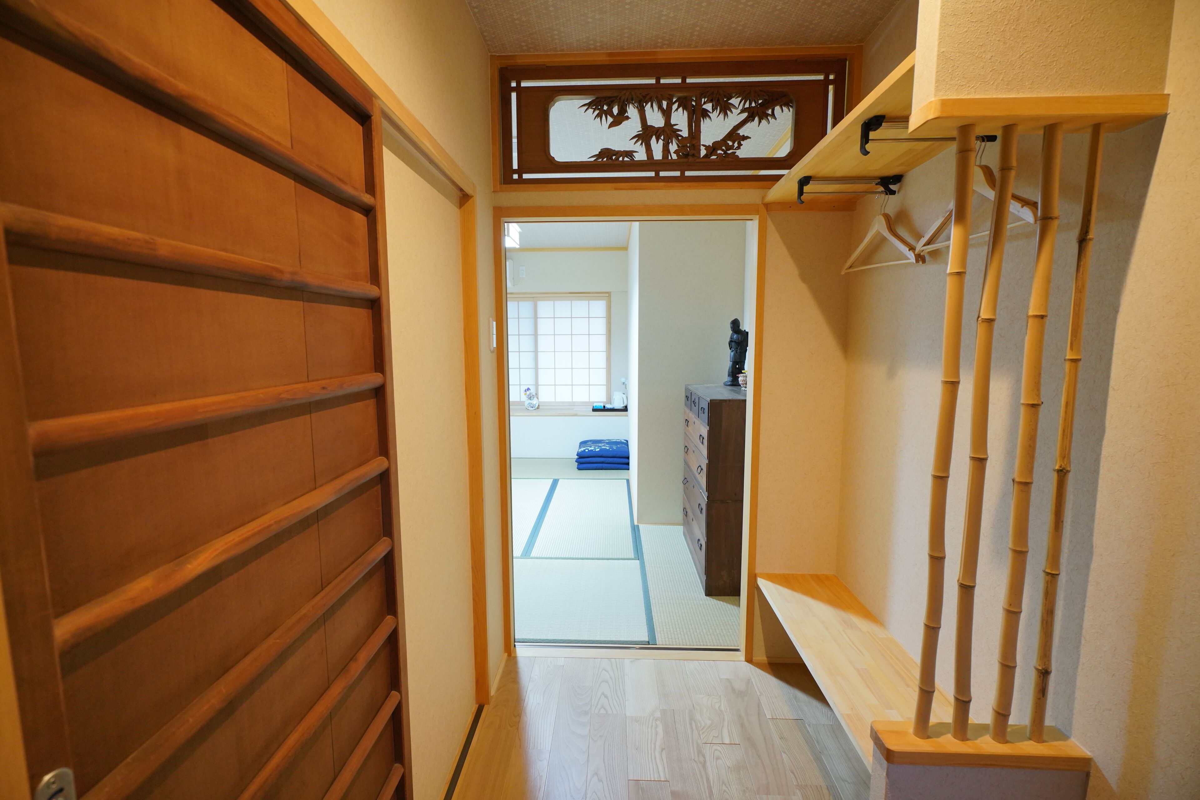 Een smalle gang met een houten deur links, een bamboe plankenset rechts, en een tatami kamer in de achtergrond.