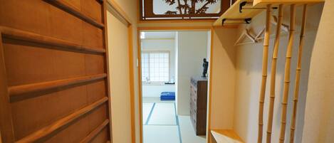 Een smalle gang met een houten deur links, een bamboe plankenset rechts, en een tatami kamer in de achtergrond.
