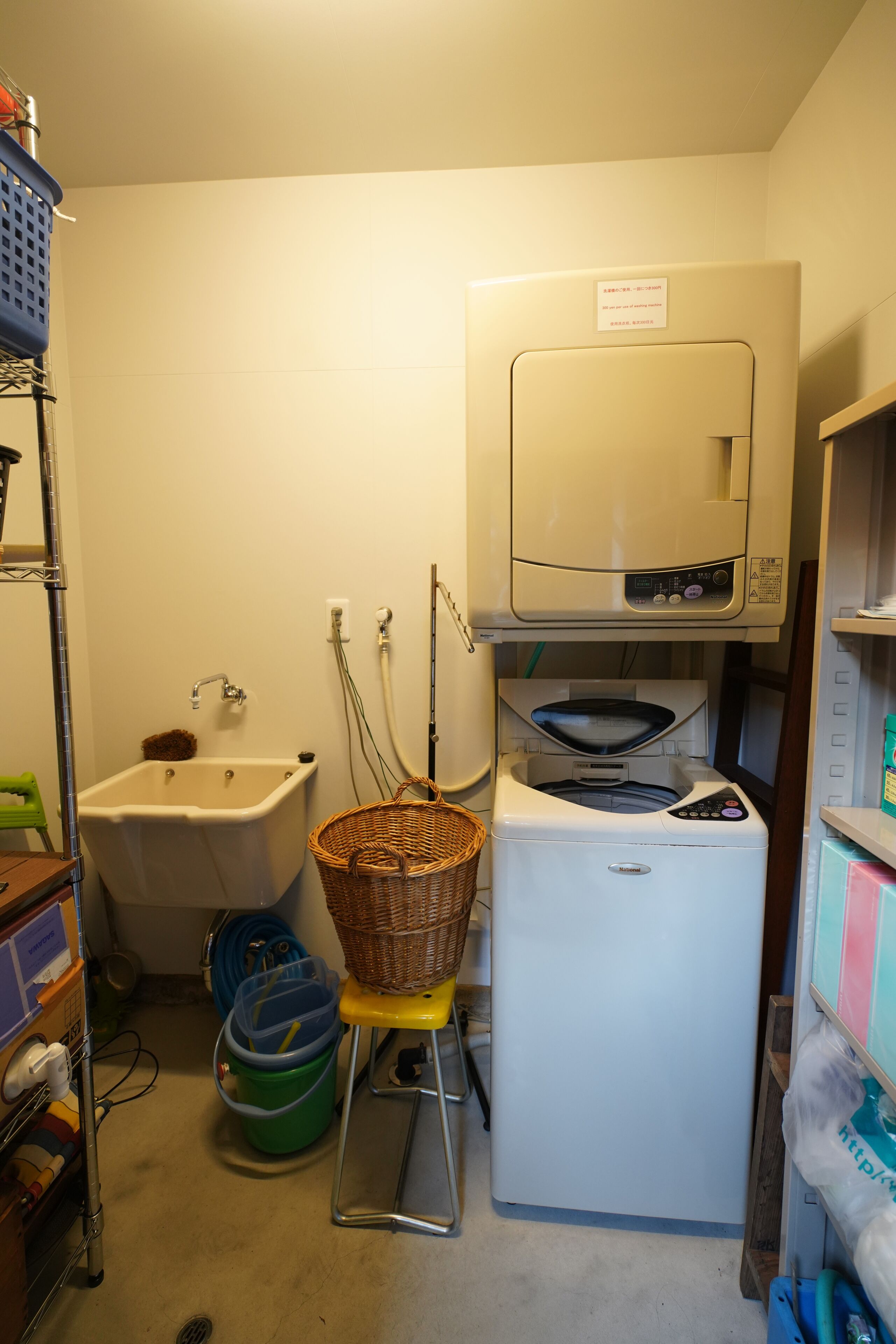 A compact laundry room with a washing machine, a sink, and a basket on a stool.