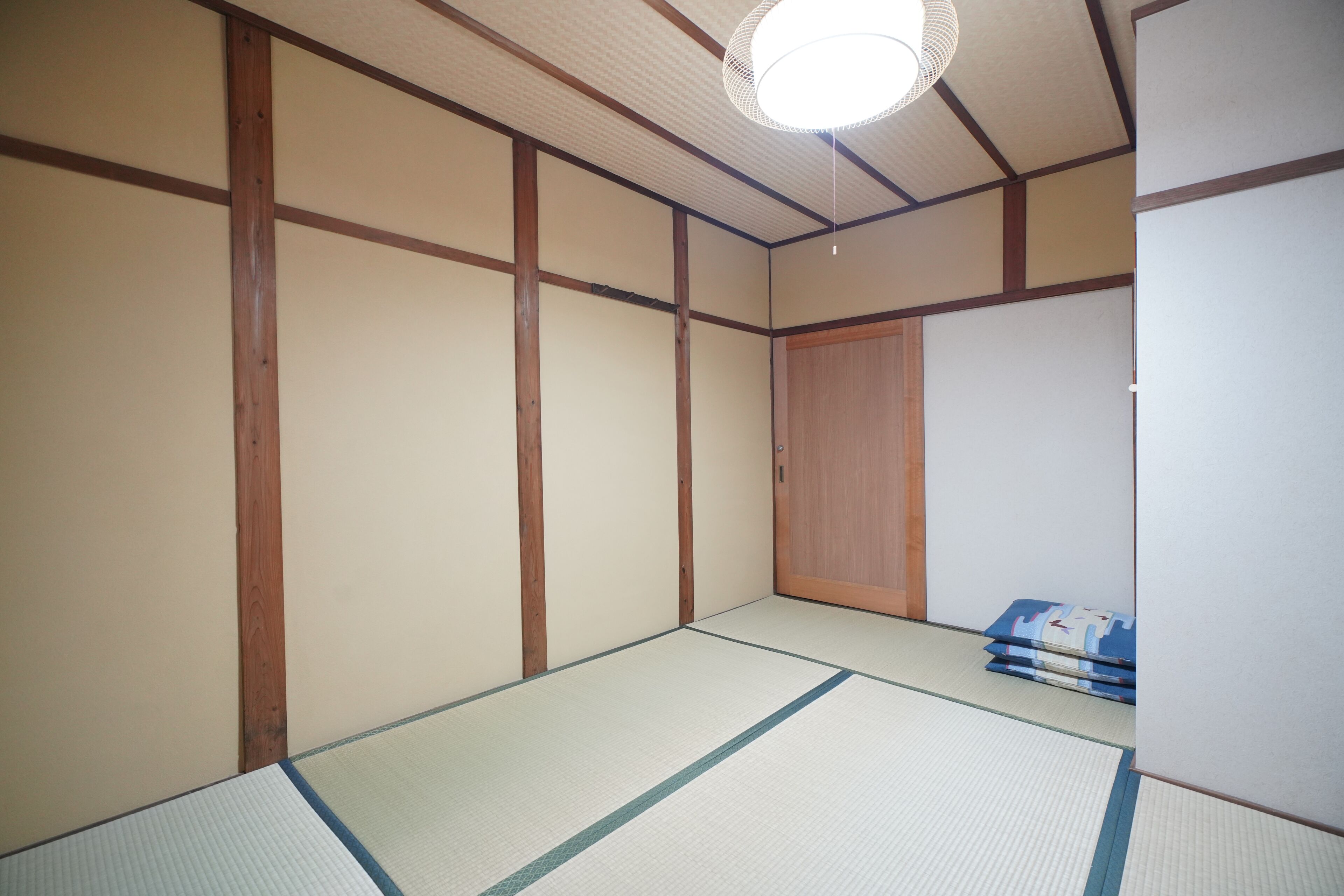 A traditional Japanese room with tatami flooring, wooden beams, and a sliding door.