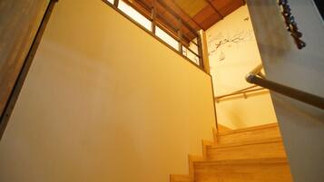 Eine Holztreppe mit Handlauf, die zu einem Raum mit Holzboden und einem an der Wand befestigten Kunstwerk führt.