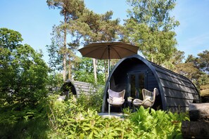A cozy, curved wooden cabin with two wicker chairs and an umbrella. - KampinaStaete (Oisterwijk)