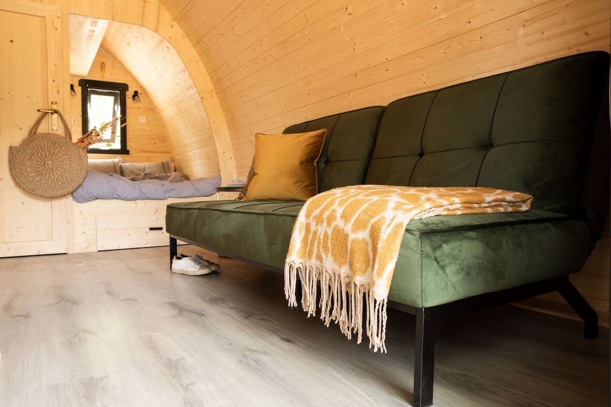 A cozy room with a green sofa, a woven basket, and a wooden ceiling.