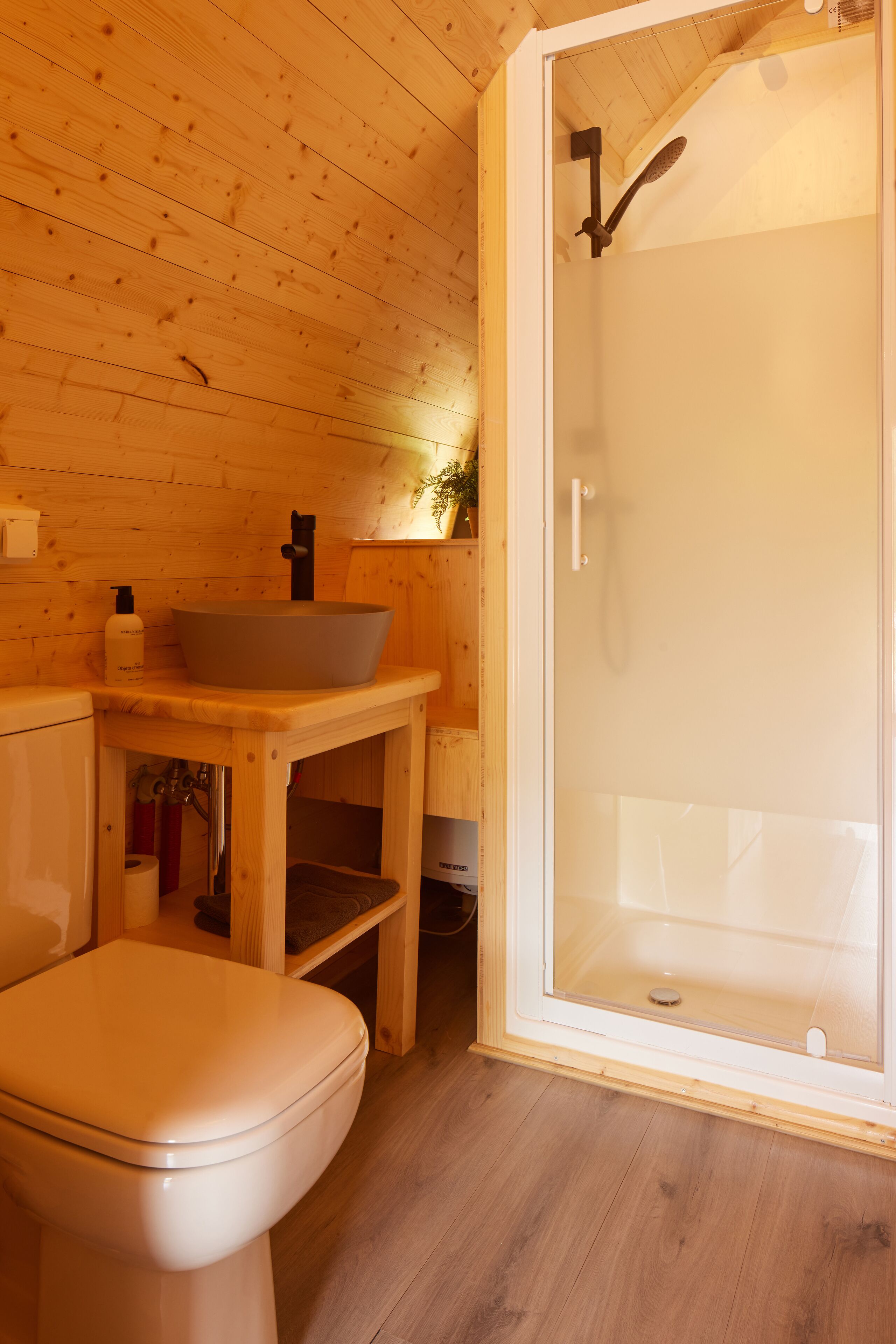 Een houten badkamer in een vakantiehuisje, met toilet, wastafel en douche.
