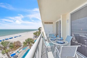 Ein Balkon mit Blick auf den Strand, ein Pool und ein Essbereich mit Tischen und Stühlen.