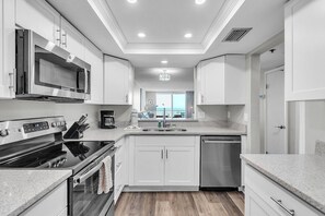 Une cuisine moderne avec des meubles blancs, des appareils en acier inoxydable et une vue sur l’extérieur.