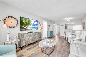 A modern living room with a flat-screen TV, a round coffee table, and a dining area with a white table and chairs.