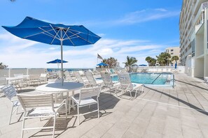 A poolside area with lounge chairs and umbrellas, a pool, and a view of the ocean.