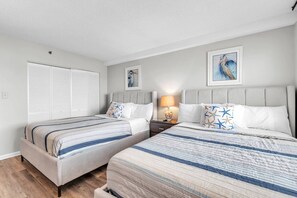 A hotel room with two beds, a nightstand with a lamp, and artwork on the walls.