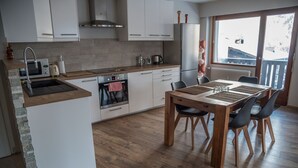 A modern kitchen with a built-in oven, a sink, and a dining area with a wooden table and chairs. - Great central location next to ski lifts and forest,spacious renovated apartment (Chamonix-Mont-Blanc)