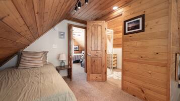 A bedroom with a wooden ceiling, a bed with a striped pillow, a nightstand with a lamp, and a door leading to another room.