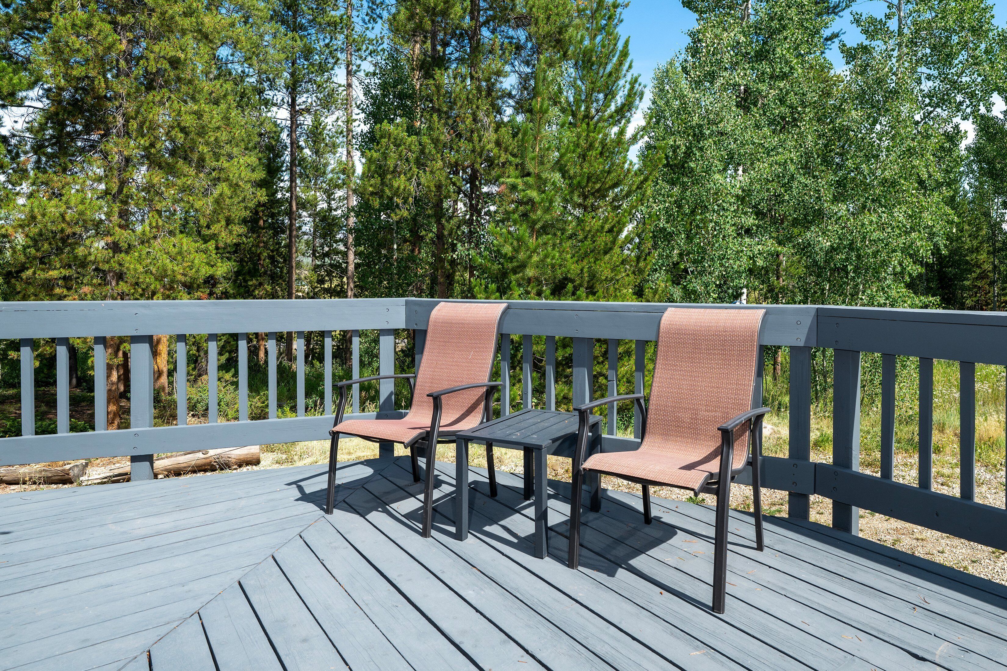 A wooden deck with two chairs and a table, surrounded by a railing and trees.