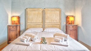Un lit double avec deux tables de chevet, chacune équipée d’une lampe, dans une pièce dont le plafond est orné de poutres en bois et les murs sont de couleur claire.