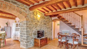 Un intérieur rustique avec des murs en pierre apparentes, des poutres en bois, un coin repas avec des chaises et un escalier.